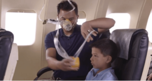 Image - airplane oxygen mask. A guardian putting a mask on a child after they have put the oxygen mask on themselves